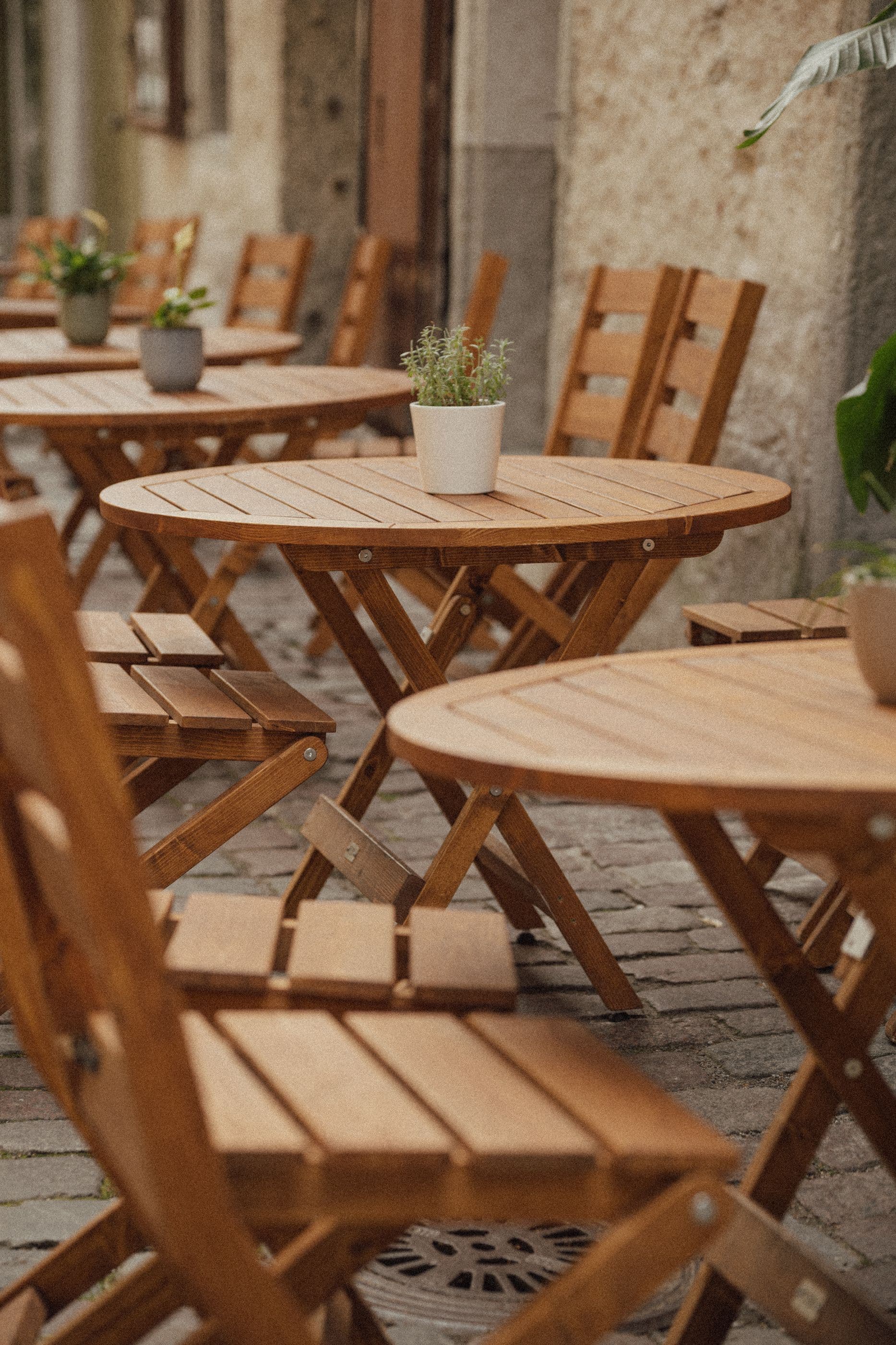 Puidubutiigi täispuidust ümmargused välilauad ja kokkupandavad toolid kohviku terrassil.